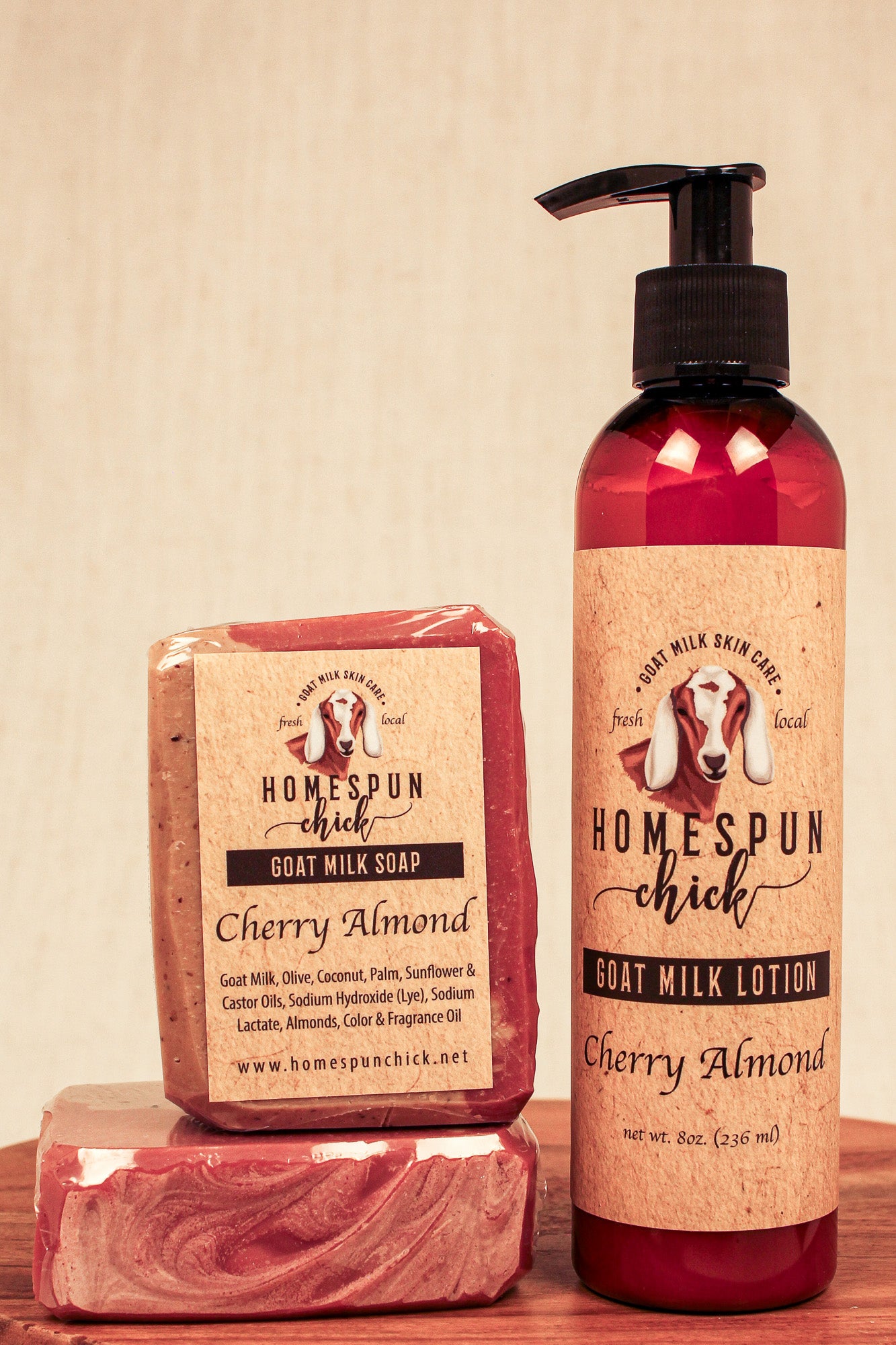 Homespun Chick Cherry Almond soap and lotion set on a wooden surface with a beige background