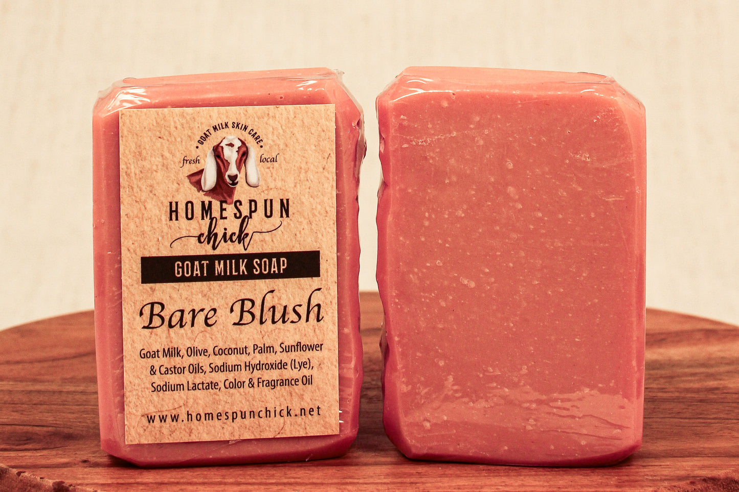 Two bars of pink goat milk soap with a label on a wooden surface.