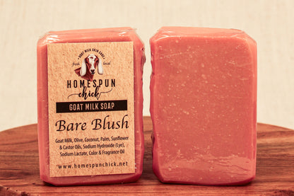 Two bars of pink goat milk soap with a label on a wooden surface.