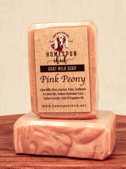 Two bars of pink goat milk soap with a visible label on a wooden surface.
