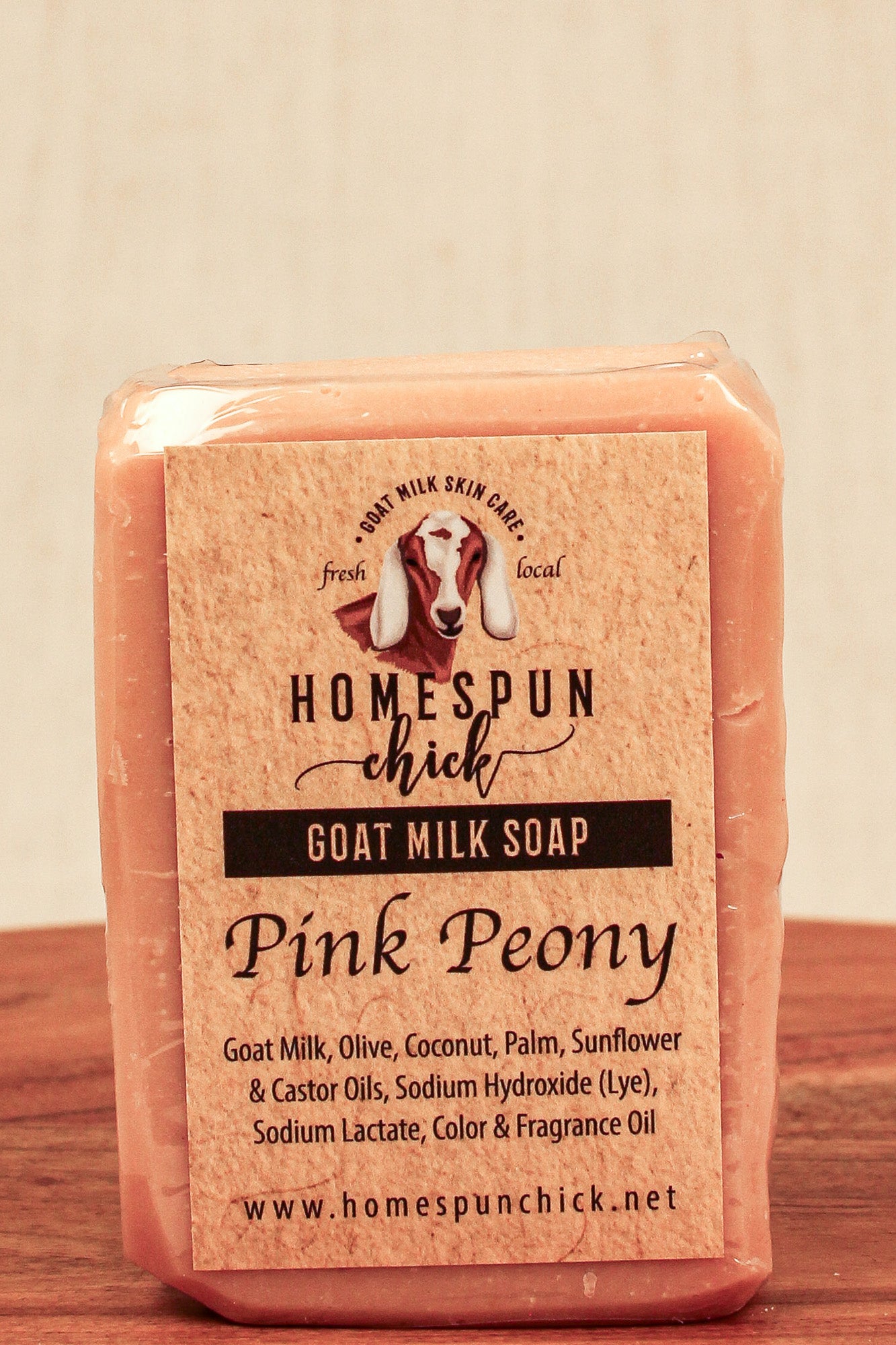 Pink goat milk soap bar with 'Homespun Chick' label on a wooden surface.
