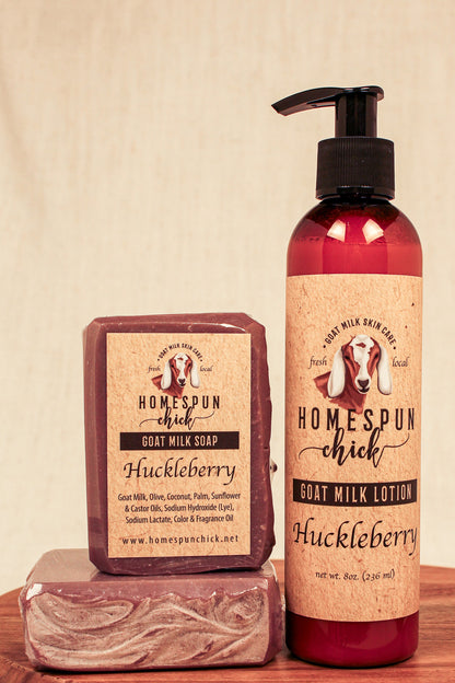 Homespun Chick Huckleberry soap and lotion on a wooden surface with a beige background